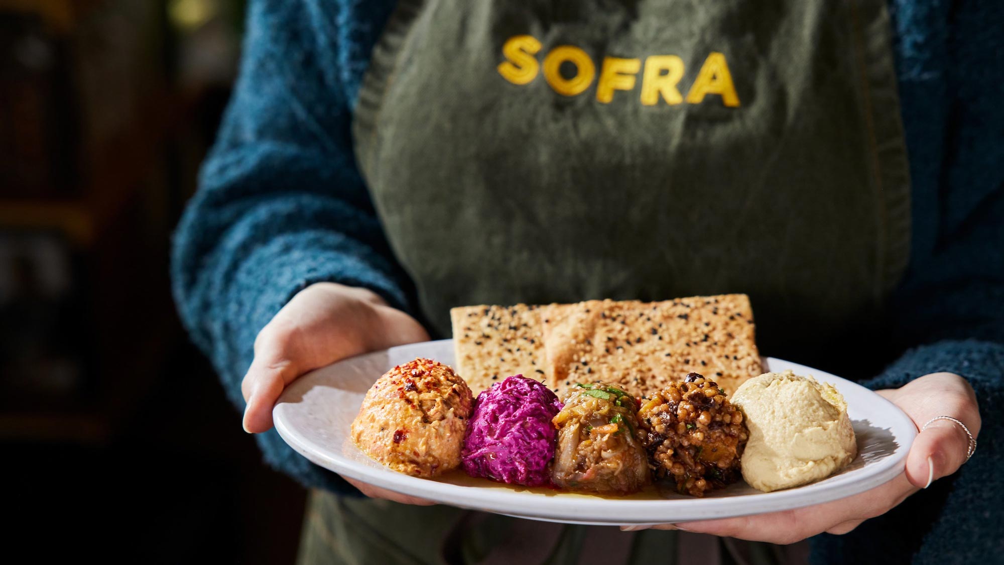 Server wearing a Sofra Bakery apron holding a plate of food